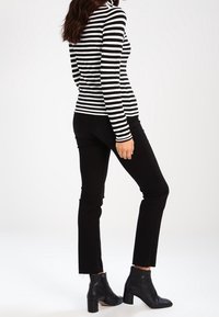 Mustavalkoraidallinen pitkähihainen paita yhdistettynä mustiin farkkuihin ja nilkkureihin. Paita on istuva ja farkuissa on lyhyt lahje.