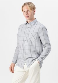 Gray checkered button-up shirt made of soft fabric, with a chest pocket and subtle tonal detailing, paired with light-colored trousers.