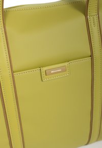 Groene synthetische handtas met een gestructureerd oppervlak, voorzien van bruine stiksels en een klein metalen label met de tekst "HEXAGONA." Glad ritsluiting.