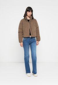 Veste rembourrée cropped en velours côtelé marron avec fermeture éclair à l'avant, dotée d'un col montant et de coutures horizontales, associée à un jean bleu évasé.