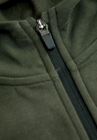 Olivgrön zip-up hoodie med en robust svart dragkedja och textiler med en slät, mjuk finish och sydda detaljer.