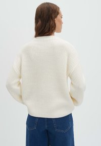 Pull en maille crème à coupe ample et texture côtelée, doté d'un col montant et d'épaules tombantes, associé à un jean large bleu marine.