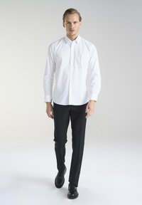 Biała koszula z długim rękawem i małym wzorem kropek, z ostro zakończonym kołnierzykiem; zestawiona z czarnymi spodniami wizytowymi i czarnymi butami.