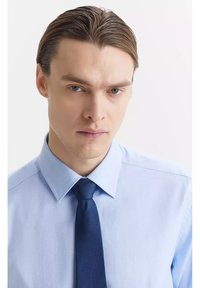 Jasnoniebieska koszula z kołnierzykiem o gładkiej fakturze, w parze z ciemnoniebieskim krawatem. Koszula ma klasyczny design z guzikami na przodzie.