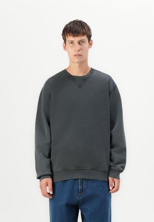Donkergrijze sweatshirt met een ronde halslijn en geribde mouwen, gemaakt van een zachte, gestructureerde stof. Gecombineerd met blauwe jeans.