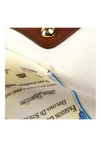 Gros plan d’un sac en tissu blanc avec garniture en cuir et une étiquette de texte imprimée à l’intérieur, partiellement visible avec des lettres bleues et noires.