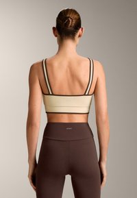 Urheiluliivit kermanvärisinä ruskeilla yksityiskohdilla ja ohuilla olkaimilla. Yhdistetty ruskeisiin korkeavyötäröisiin legginsseihin. Sileä, joustava kangas.