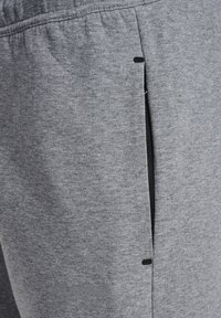 Primer plano del bolsillo de unos pantalones deportivos grises con un logo de marca sutil y cinturilla elástica, destacando la textura de la tela y los detalles de las costuras.