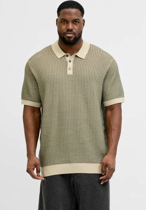 Uomo che indossa una polo a maniche corte in maglia beige con motivo, collo e tre bottoni, abbinata a pantaloni scuri su sfondo chiaro.