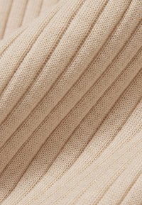 Close-up van beige geribbelde gebreide stof met gedetailleerde verticale textuur en stiksels.