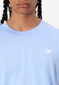 T-shirt en coton bleu clair avec un col rond, arborant un petit logo "NB" blanc sur la poitrine. Texture douce et coupe régulière.