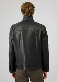 Zwarte leren jas met een staande kraag, gestructureerde afwerking en knopen op de mouwen; heeft een rechte achterkant.