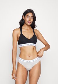 Bralette noire avec un décolleté en V et des bretelles larges ; culotte hipster grise avec une bande blanche affichant le logo "GUESS". Tissu en mélange de coton lisse.
