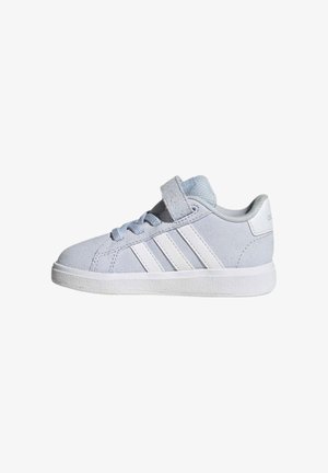 Zapatilla Adidas de color gris claro con rayas blancas, cierre de velcro, cordones y suela texturizada, mostrada de lado sobre un fondo blanco.