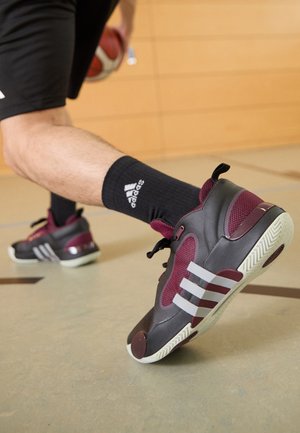 Basketballschuhe in grau und kastanienbraun, mit Mesh-Details und drei weißen Streifen. Schwarze Knöchelsocken mit sichtbarem Logo.