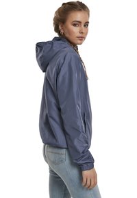 Giacca leggera e impermeabile con cappuccio in blu ardesia opaco, dotata di polsini elasticizzati, tasche laterali con zip e un fit rilassato.