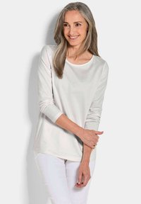 Helles graues Langarmoberteil mit einem Boot-Ausschnitt, glatter Textur und sanfter Drapierung, kombiniert mit weißen Hosen. Einfaches und vielseitiges Design.