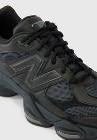 Must ja hall New Balance toss võrgust detailide, paksu polsterdatud tallaga ning silmapaistva "N" logoga küljel, nähtud nurga alt suumitud lähivaates.