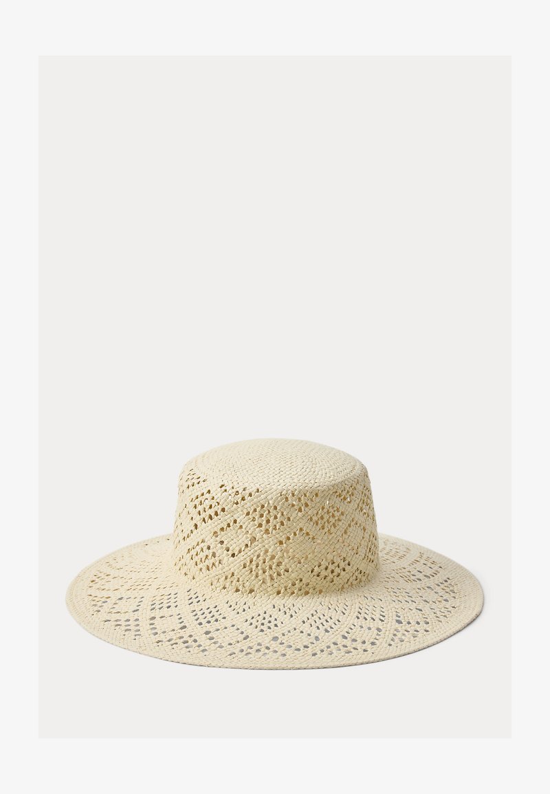 Πλατύγυρο μπεζ ψάθινο καπέλο με υφαντό, διακοσμητικό σχέδιο και επίπεδη κορώνα στην κορυφή, απεικονιζόμενο σε απλό φωτεινό φόντο.