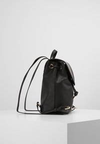 Mochila de cuero sintético negro con forma redondeada, correas de hombro ajustables y detalles en metal dorado. Presenta una tapa plegable.