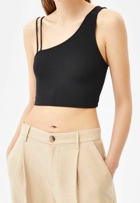 Černý žebrovaný crop top s asymetrickým výstřihem a tenkými ramínky, spárovaný s béžovými kalhotami s vysokým pasem, které mají zapínání na knoflík.