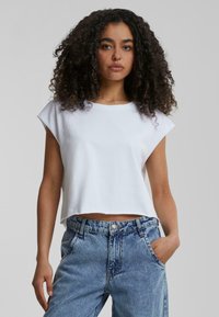 Fehér, rövid ujjú, cropped póló, pamutból készült. Világoskék, magas derekú farmernadrággal párosítva, amelyen kopott minta található.