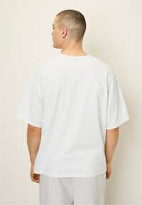 White cotton T-shirt with a relaxed fit, dropped shoulders, and short sleeves. Smooth texture and visible stitching details at hem.