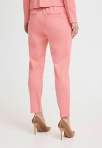 Rosa, figurbetonte Hose mit weicher Textur, elastischem Bund und zwei Gesäßtaschen, kombiniert mit braunen High Heels.