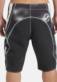 Άνδρας με μαύρα και διακοσμημένα σορτς για σέρφ, από πίσω, με μπλε και λευκές ραφές και αφηρημένο σχεδιασμό με σημεία.