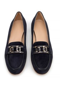 Marineblaue Wildlederslipper mit rechteckigem Metallelement, runder Spitze und kontrastierender Naht entlang der Kanten. Weiche Innenausstattung.