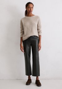 Beżowy sweter o teksturowym wzorze z długimi rękawami, zestawiony z czarnymi, skórzanymi spodniami typu wide-leg, charakteryzującymi się gładkim wykończeniem i subtelnym blaskiem. Brązowe buty wsuwane.
