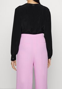 Blusa nera in satin con maniche lunghe e polsini abbottonati, abbinata a pantaloni a gamba larga rosa chiaro a vita alta con tasche posteriori.