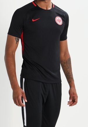 Mann trägt schwarzes und rotes Sporttrikot mit Eintracht Frankfurt-Logo und passende schwarze Hose mit weißen Streifen.