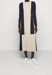 Jurklang met lange mouwen in beige met donkerblauwe accenten. Gemaakt van zachte stof, met een rechte snit en zijslits, gecombineerd met witte sneakers.