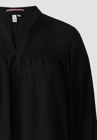 Blouse noire à manches longues avec col en V, détails froncés sur la poitrine et coupe décontractée.