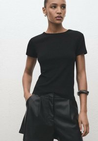 Black short-sleeve t-shirt with a round neckline, paired with black pleated leather shorts. Smooth texture, minimalistic design.