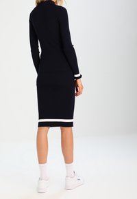 Laivastonsininen ribbed neulemekko, jossa on istuva siluetti ja valkoiset raidat helmassa ja hihoissa, yhdistettynä valkoisiin tennareihin.