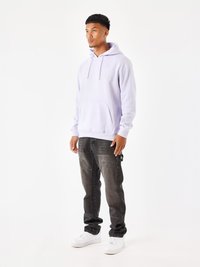 Sudadera de color púrpura claro con cordones y bolsillo frontal, combinada con jeans de lavado oscuro y zapatillas blancas. Diseño minimalista y ajuste relajado.