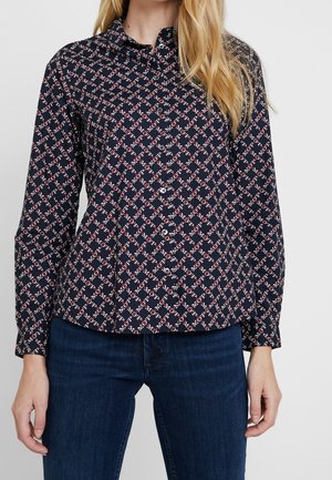 Marineblaues Hemd mit geometrischem rot-weißen Muster, langen Ärmeln, Kragen und leichtem Stoff, kombiniert mit dunklen Jeans.