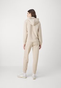 Beige hoodie och jogger-set av mjukt tyg med ribbade mudd. Har en huva och elastisk midja, utformat för komfort och bekvämlighet.