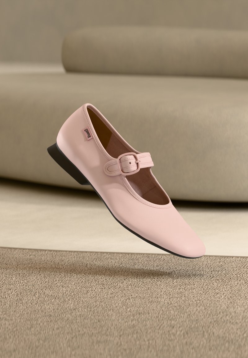 Ροζ δερμάτινο γυναικείο παπούτσι Mary Jane με τετράγωνη μύτη, ρυθμιζόμενο λουράκι και αγκράφα, χαμηλό μαύρο τακούνι και απαλό υφή, αιωρούμενο πάνω από χαλί.