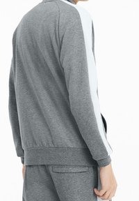 Grijs atletiekjack met witte zijstrepen, een ronde kraag, geribde manchetten en een aansluitende tailleband, gemaakt van een zachte, gestructureerde stof.