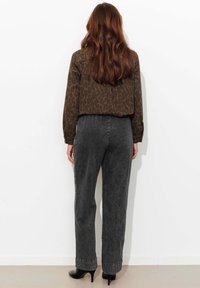 Blouse à imprimé léopard marron associée à un pantalon en jean gris à jambes larges et des chaussures noires à talons hauts. Cheveux coiffés en ondulations lâches.