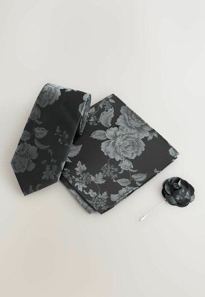 Black tie set features a floral pattern in silver, including a tie, pocket square, and a fabric flower lapel pin, all in a smooth finish.