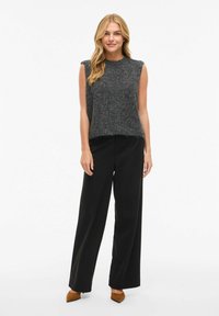 Pelēks bezroku džemperis ar apaļu izgriezumu, kombinēts ar melnām platām biksēm un brūnām apavām ar smailu purngalu. Gluda tekstūra un brīvs piegrieziens.