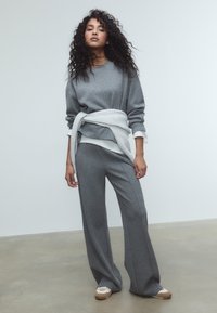 Sivý pletený sveter s voľným strihom, skombinovaný s vysokými nohavicami v rovnakom odtieni. Svetlosivý detail je zviazaný v páse. Silueta s širokými nohavicami.