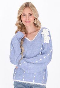 Gaiši zils v-veida džemperis no pūkaina materiāla, ar baltajiem izšuvumiem un ziedu akcentiem uz pleca. Mīksta tekstūra un brīva piegriezuma.