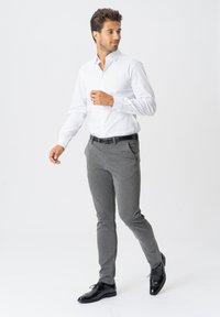 Hvid langærmet skjorte, grå skræddersyede bukser, sort bælte og sorte snøresko. Glat tekstur med et tætsiddende design.