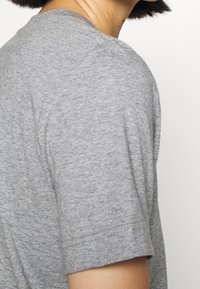 Grå kortærmet T-shirt lavet af blødt, tekstureret stof med rund halsudskæring, der har en afslappet pasform og synlige syninger.