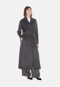Cappotto lungo in lana grigia, con cintura, ampi revers e tasche laterali. Ha una lunghezza fino al polpaccio e un taglio dritto. Design su misura, accenti minimali.